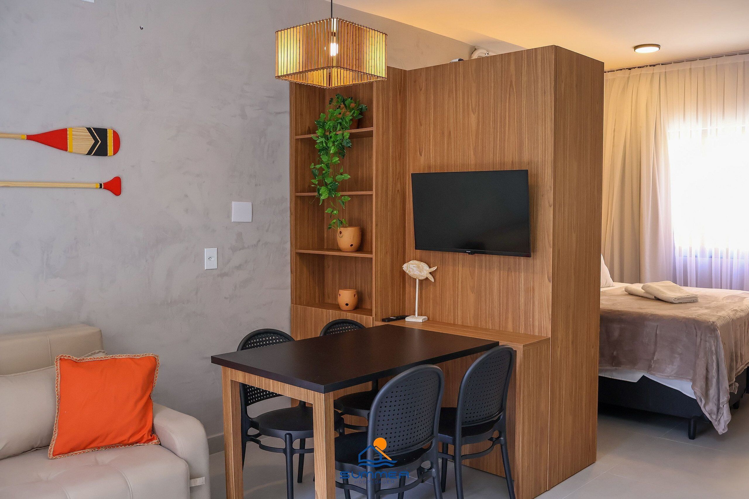Un espace de vie compact avec une cloison en bois, un téléviseur fixé au mur, une table à manger avec des chaises, un canapé et un lit.
