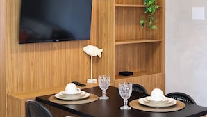 A dining area with a flat-screen TV mounted on a wooden wall, a white fish sculpture, and a potted plant. - Condominio Petit (TIBAU DO SUL)