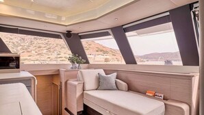 A compact interior with a sofa, a small table, and a window offering a desert view. - Floating Villa: Yacht Vacation with Captain & Chef - 10 Guests - 66 Ft (Άλιμος)