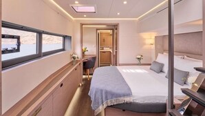 A modern hotel room with a bed, bedside table, desk, chair, and a window with a view. - Floating Villa: Yacht Vacation with Captain & Chef - 10 Guests - 66 Ft (Άλιμος)