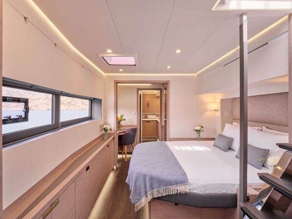A modern hotel room with a bed, bedside table, desk, chair, and a window with a view.