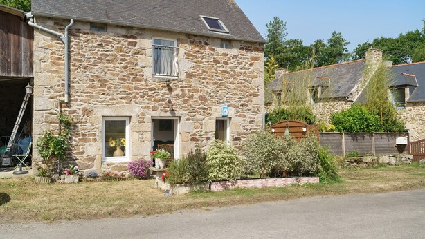 Ein Haus aus Stein mit Garage, einem kleinen Fenster und einem Garten mit verschiedenen Pflanzen.