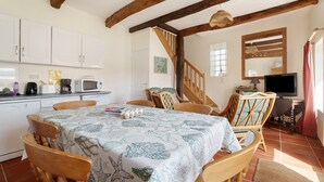 Ein Essbereich mit einem Tisch für vier Personen, Holzstühle, eine Küche mit weißen Schränken, eine Holztreppe und ein Fernseher.