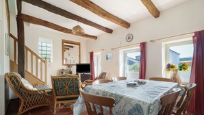 Ein Essbereich mit einem Tisch für vier Personen, Holzsesseln, einem Fernseher und einem Fenster mit Vorhängen.
