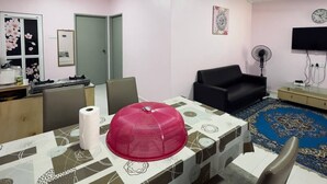 A room with a dining table, chairs, ceiling fans, a black sofa, a TV, and a patterned rug. - 2-bedroom house 170 metre Seaview Homestay enchanting Mersing with swimming pool (Mersing)