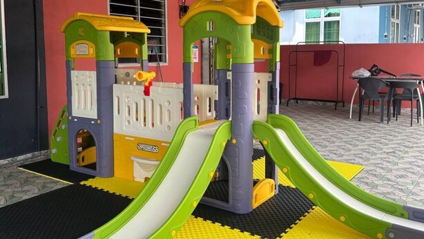 A children's play area with slides and climbing structures, set on a tiled floor with a red wall and a metal roof. - 2-bedroom house 170 metre Seaview Homestay enchanting Mersing with swimming pool (Mersing)