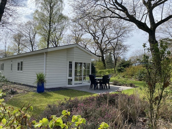 Ein eingeschossiges Haus mit Terrasse, umgeben von einem Garten und Bäumen.