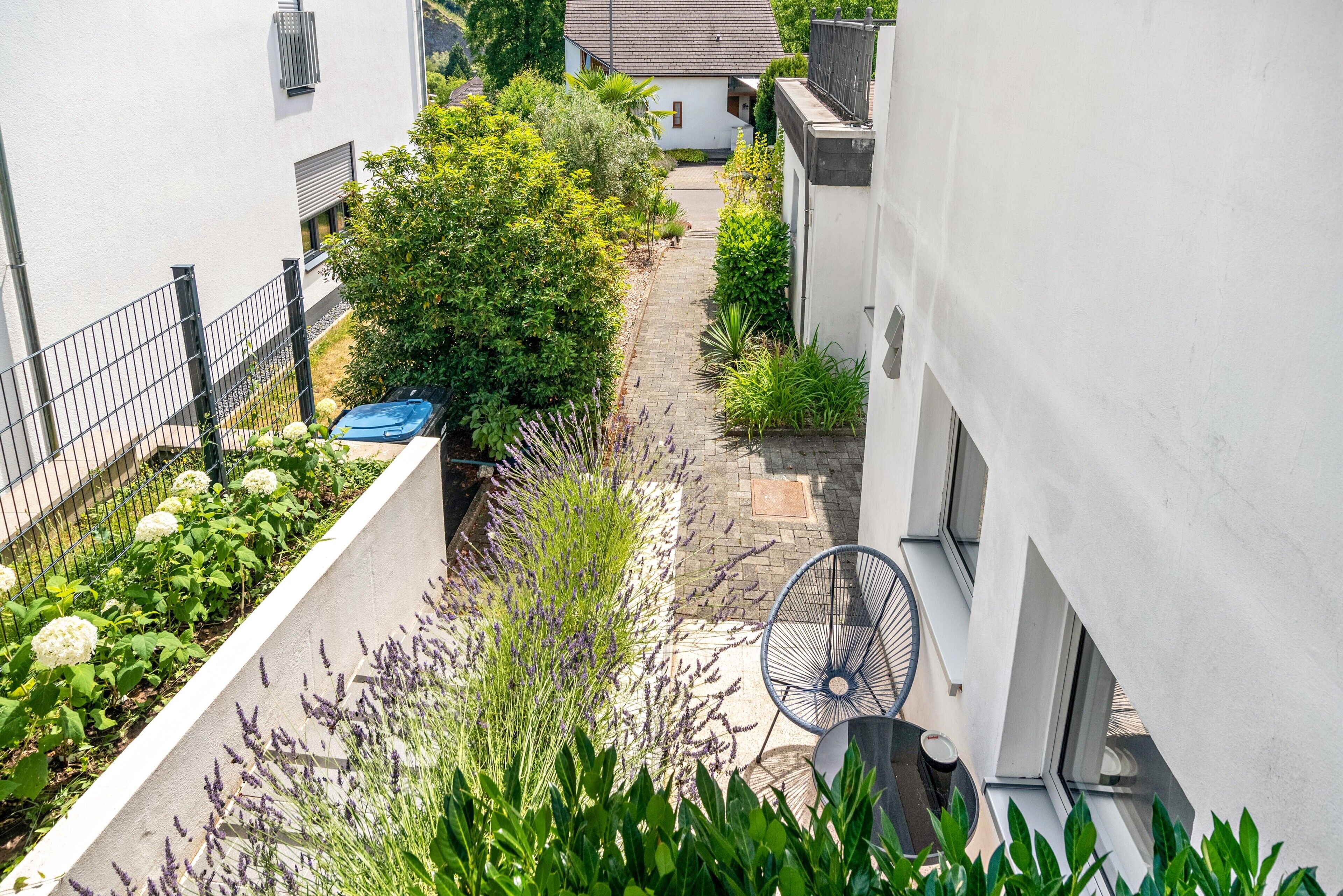 Une ruelle étroite avec un jardin, une chaise bleue et un bâtiment blanc.