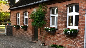 En murstensbygning med mange vinduer, enkelte med blomsterkasser, og en brostenbelagt gårdsplads.