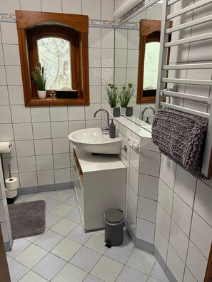 Une salle de bain avec un lavabo blanc, un miroir, un porte-serviettes et des plantes en pot.