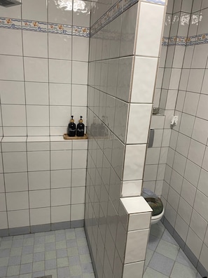 A bathroom with white tiles, a toilet, and two bottles on a shelf.
