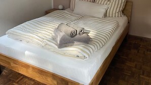 En pænt redt seng med stribet sengetøj og puder, et træhovedgærde og et vævet trægulv.