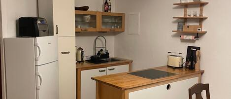 A compact kitchen with a refrigerator, a sink, a wooden countertop, and a dining area with a chair.