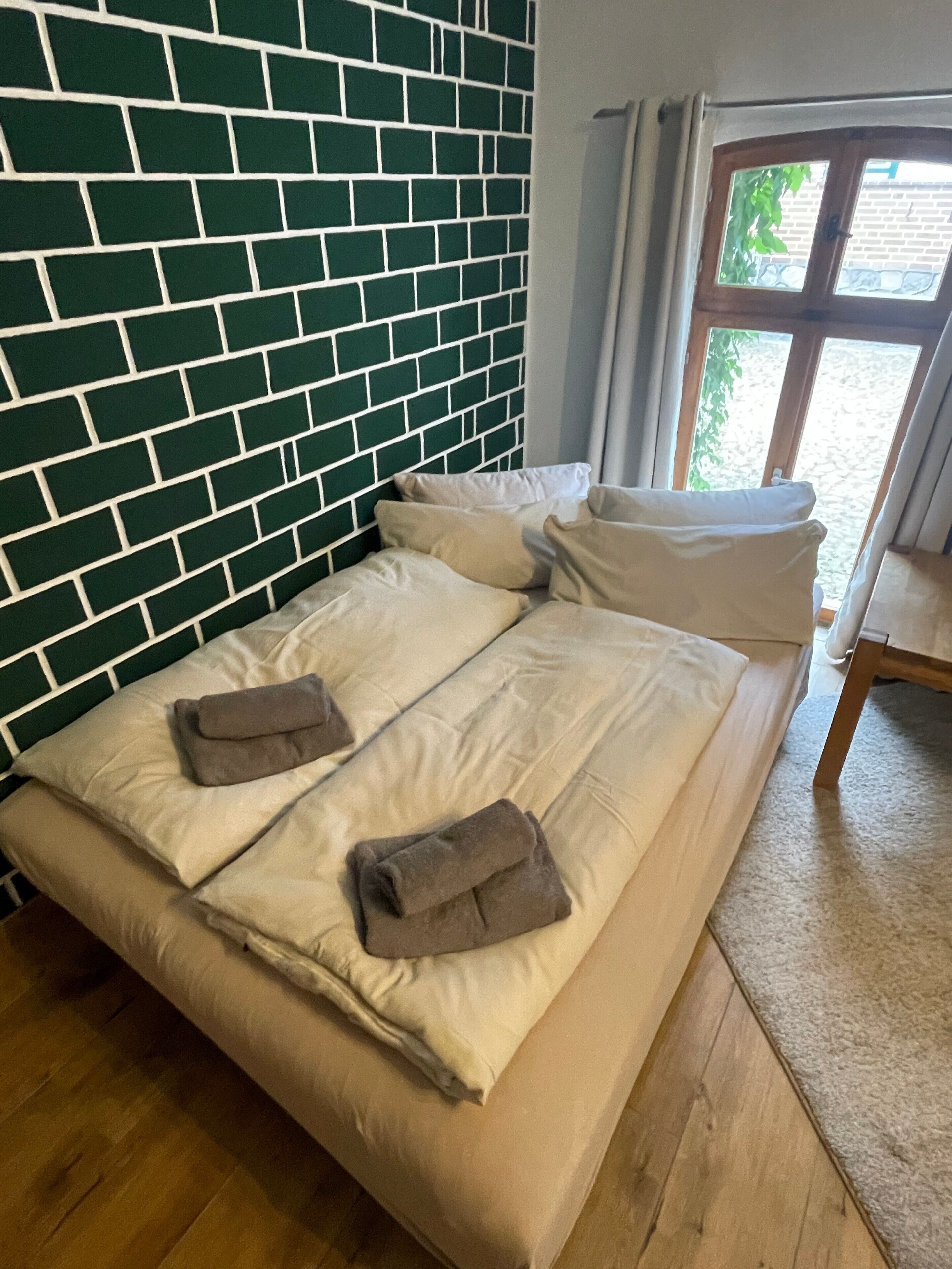 A bed with a green brick wall behind it, a window with curtains, and a wooden floor.