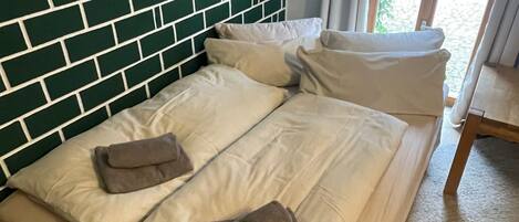 A bed with a green brick wall behind it, a window with curtains, and a wooden floor.