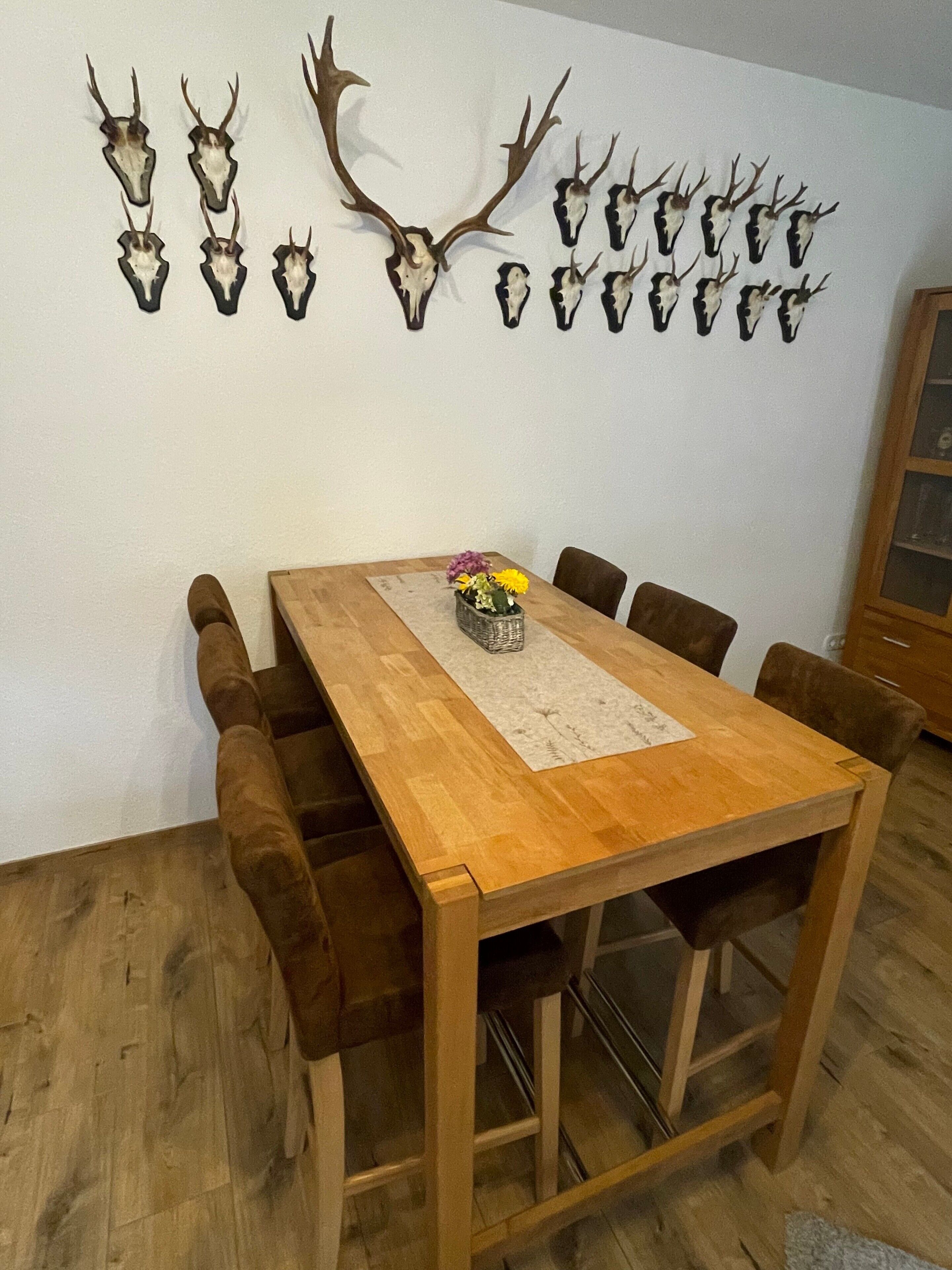 A dining area with a wooden table, chairs, and a wall-mounted deer skull display.