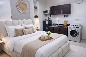 Een moderne slaapkamer met een groot bed, een wasmachine en een keukenhoek.