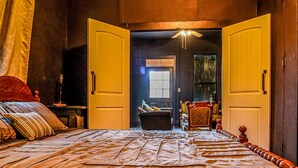 Een kamer met een bed, een tafel, stoelen en een open deur naar een andere kamer.