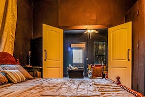 Ein Zimmer mit einem Bett, einem Tisch, Stühlen und einer offenen Tür zu einem anderen Raum.