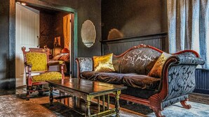 Een kamer met een donkergrijze bank, een houten salontafel en een fauteuil met een patroon.