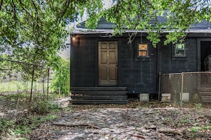 A small, dark wooden building with a single door and a small window, surrounded by a chain-link fence and trees. - Frenchmen - New Orleans (New Orleans)