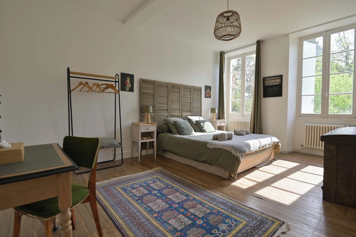 Een slaapkamer met een bed, een bureau, een stoel, een hanglamp en een raam.