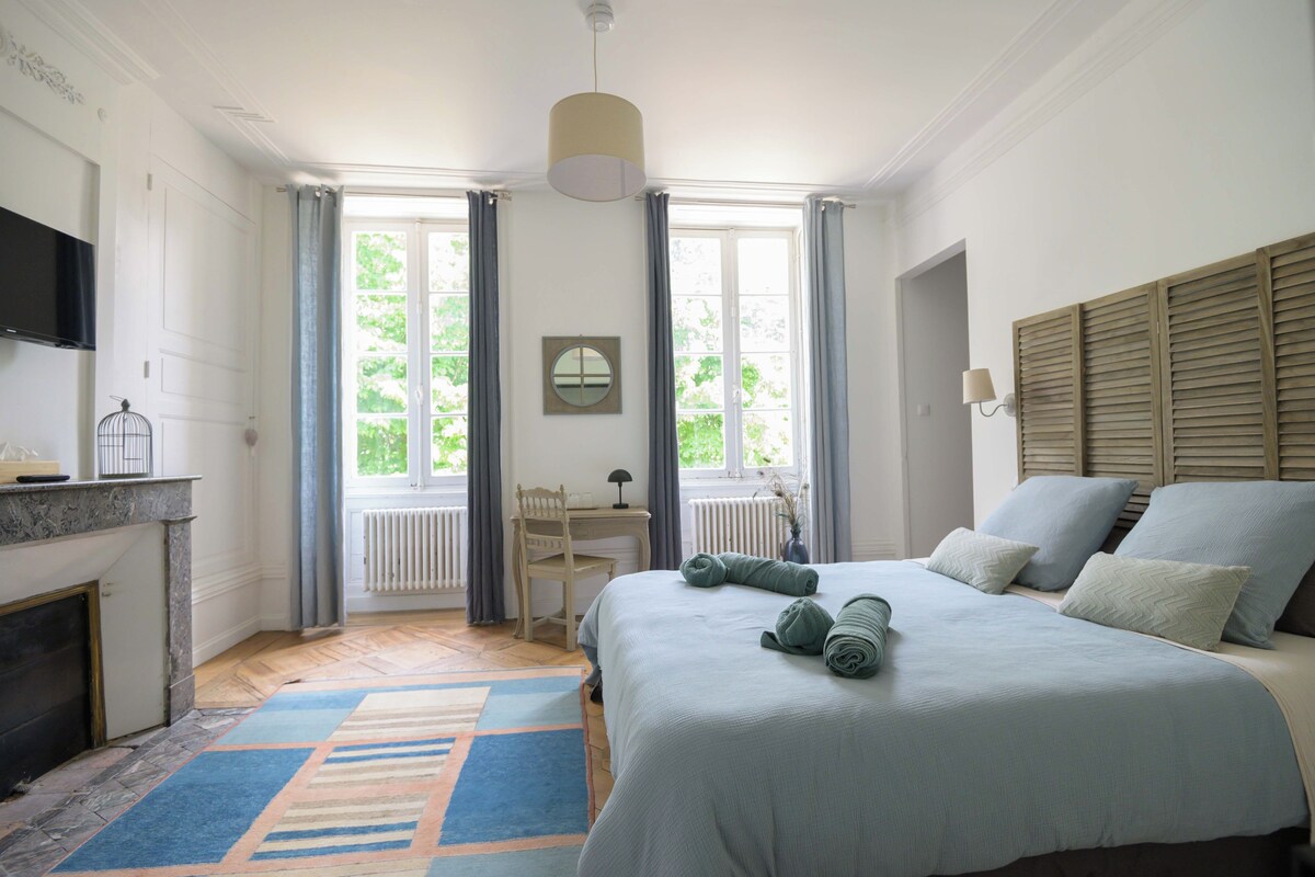 Een slaapkamer met een bed, een bureau, een stoel, een radiator, een televisie en een raam met gordijnen.