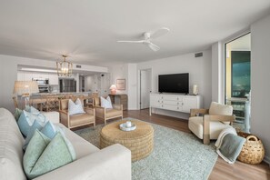 Ein modernes Wohnzimmer mit einer Couch, Sesseln, einem Couchtisch, einem Fernseher und einem Essbereich im Hintergrund.