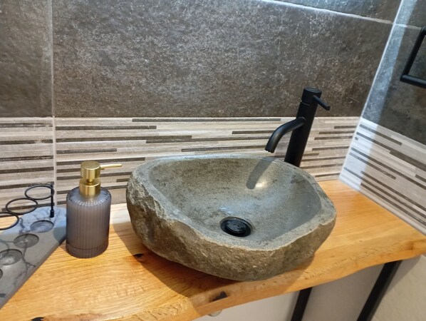 Un lavabo in pietra con un rubinetto nero, una bottiglia di sapone e un piano d'appoggio in legno.