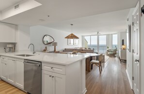 A modern kitchen with a central island, a dining area with a sofa, and a view of the ocean. - Beautifully Designed Oceanfront Villas Close to Everything (Folly Beach)