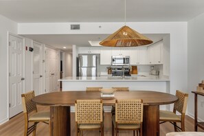 Une cuisine moderne avec des meubles blancs, des appareils en acier inoxydable et un coin repas comprenant une table en bois et des chaises en osier.