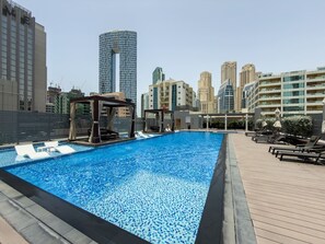 Une piscine sur le toit, dotée de chaises longues et d’une pergola, le tout entouré d’immeubles de grande hauteur.
