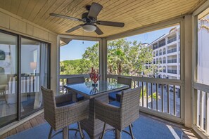 A covered balcony with a glass table, wicker chairs, and a ceiling fan.