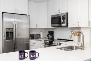 A modern kitchen with white cabinetry, stainless steel appliances, a microwave, toaster, coffee maker, and a sink. - Charming Ocean View Condo in Wild Dunes (Isle Of Palms)