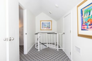 A room with a white door, a white railing, a framed painting on the wall, and patterned carpet. - Charming Ocean View Condo in Wild Dunes (Isle Of Palms)