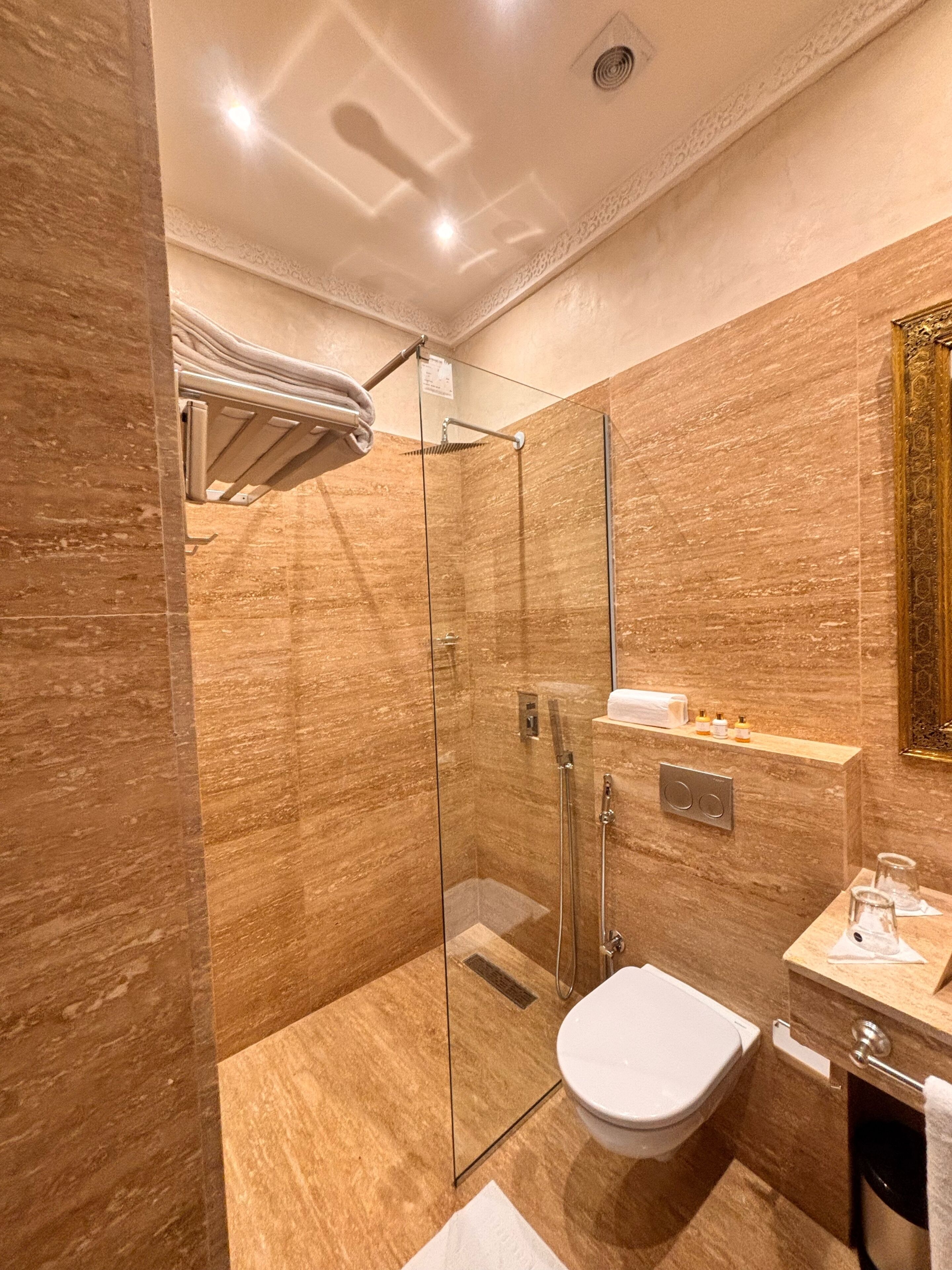 A modern bathroom with a glass-enclosed shower, a white toilet, and a marble-tiled wall.