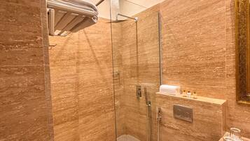 Un baño moderno con ducha envuelta en vidrio, inodoro blanco y pared con azulejos de mármol.