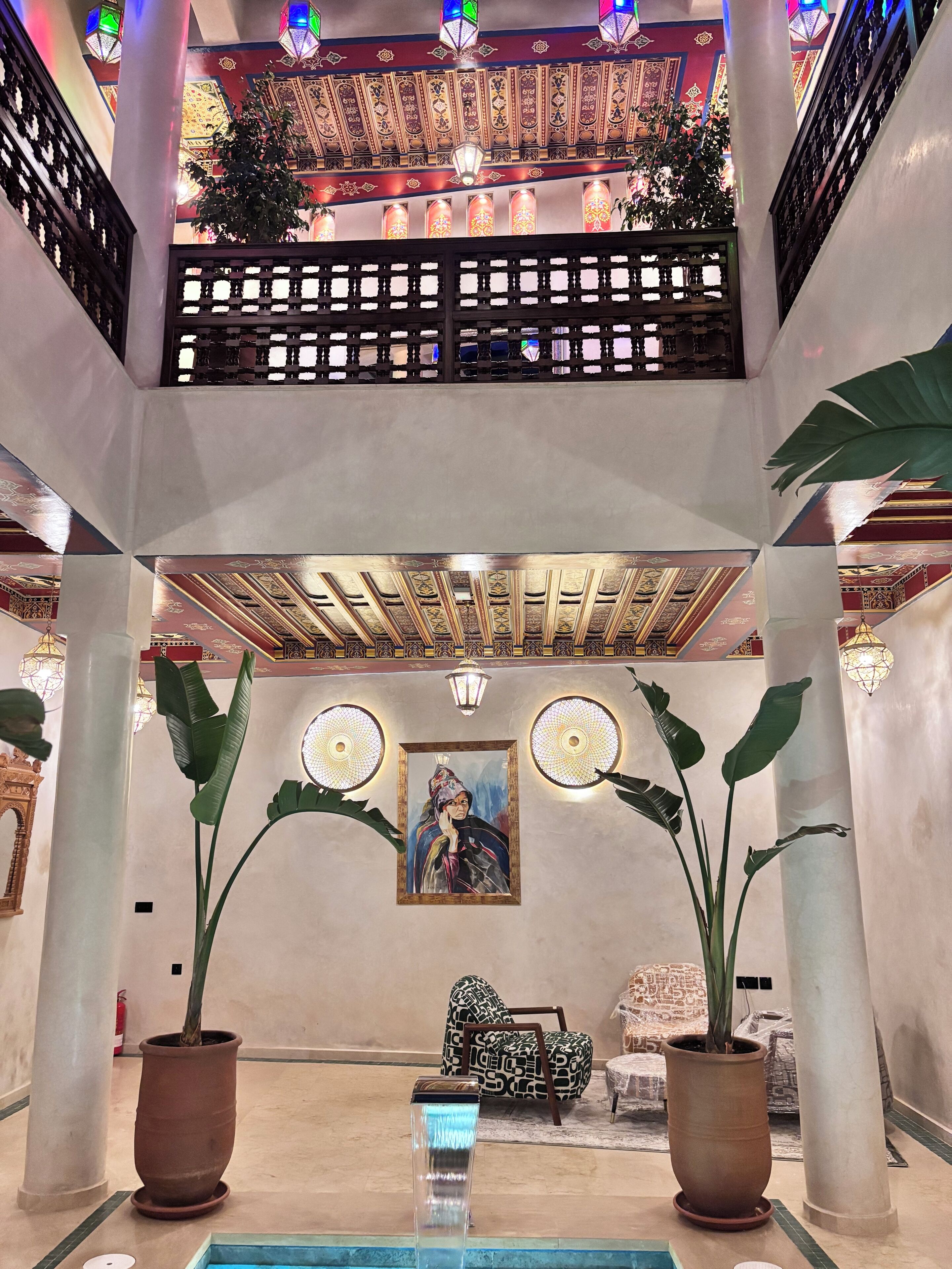 Eine Lobby mit hoher Decke, dekorativen Laternen, einem zentralen Gemälde und Topfpflanzen.