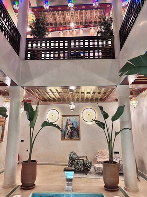 Un vestíbulo con techo alto, faroles decorativos, un cuadro central y plantas en macetas.
