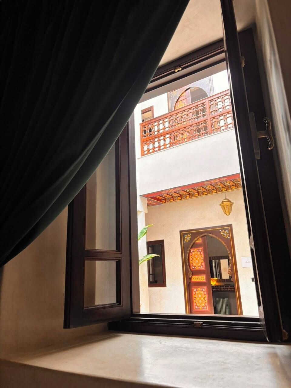 Una ventana abierta con vistas a un edificio tradicional con balcón y puertas ornamentadas.