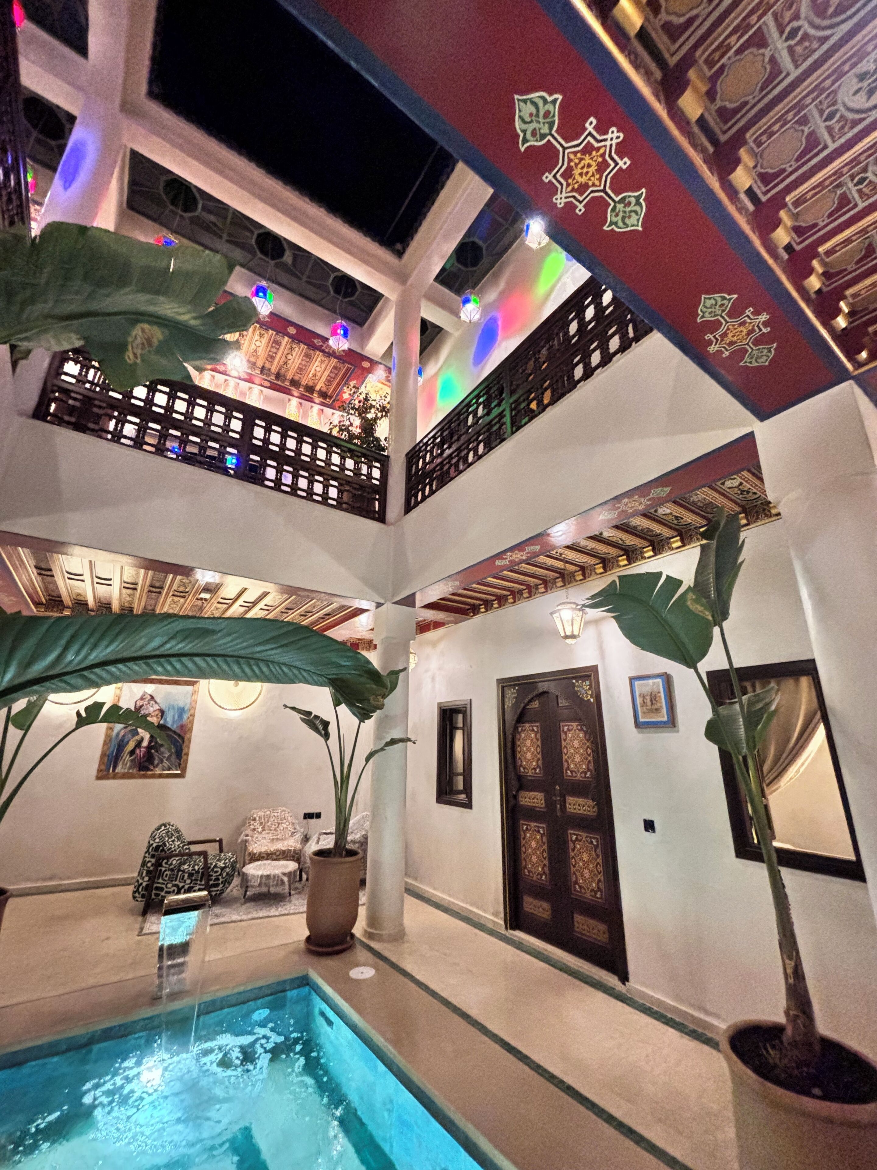 A multi-level indoor space with a pool, potted plants, and ornate doors.