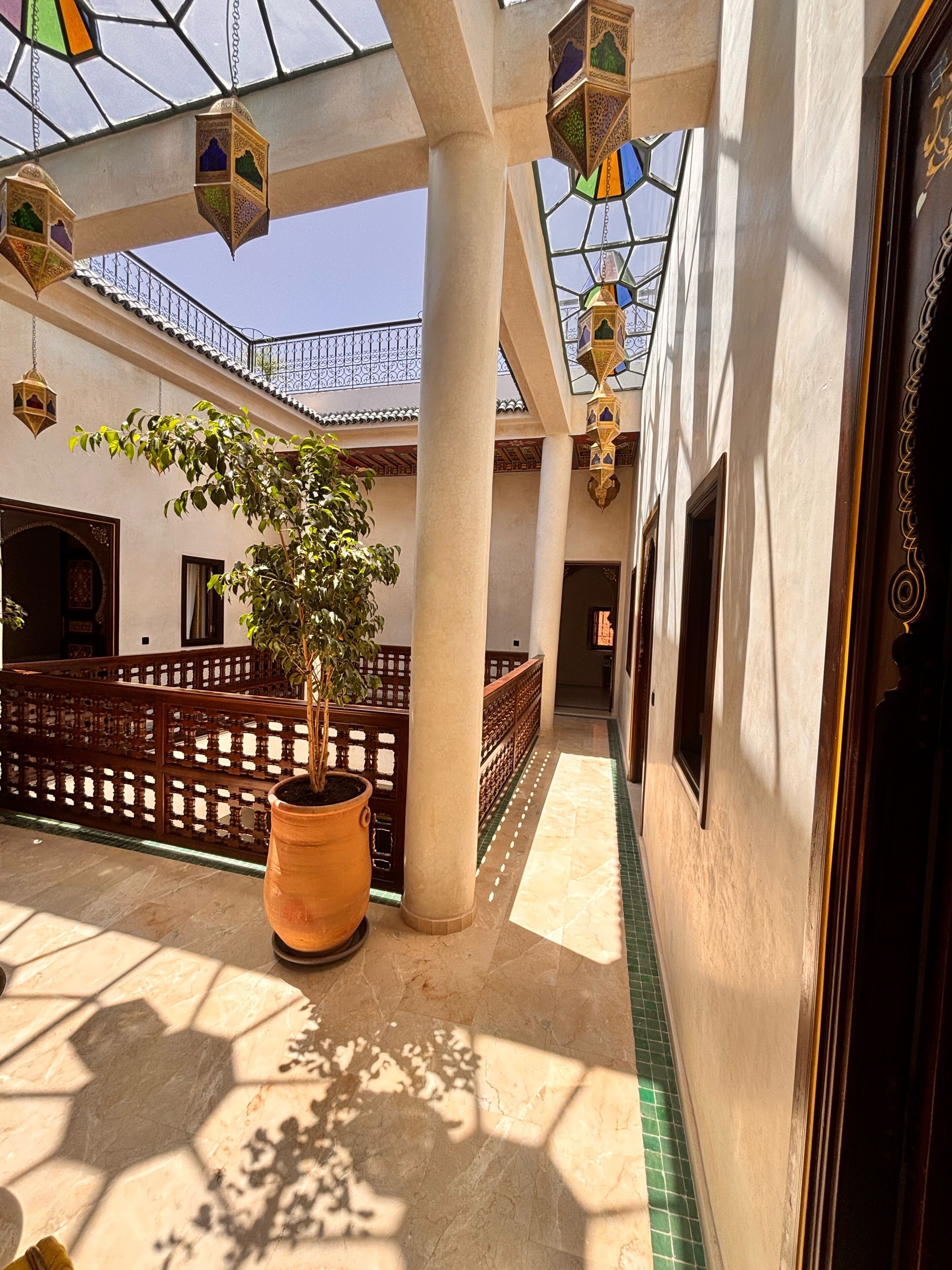 A corridor with a potted plant, columns, and a tiled floor.