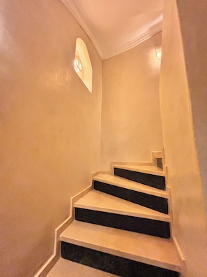 A staircase with a light fixture at the top and a small window on the wall.