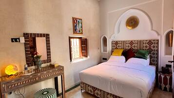 Habitación de hotel con cama, tocador con espejo, aire acondicionado de pared y cabecero estampado.