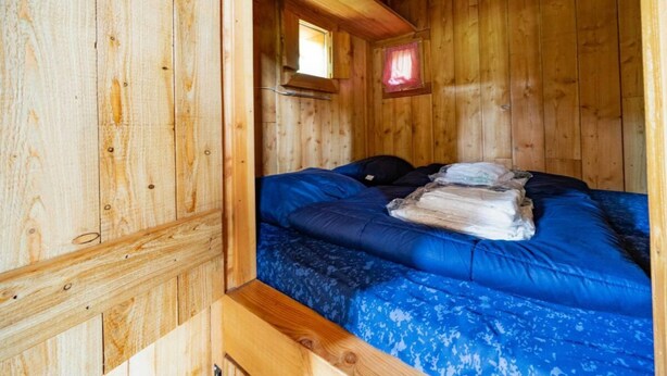 Ein Zimmer in einer Holzhütte mit einem Bett, einem Fenster und einer kleinen roten Leuchte.