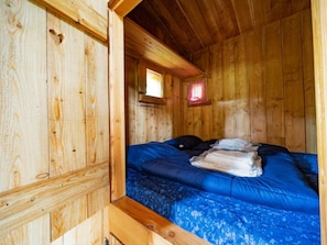 Ein Zimmer einer Holzhütte mit einem Bett, einem Fenster und einer kleinen roten Leuchte.
