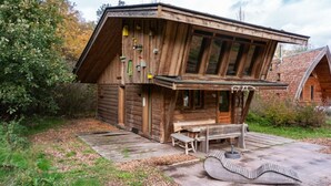 Eine Holzhütte mit geneigtem Dach, einer Holzterrasse und einer Bank.