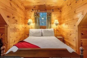 Ein Zimmer in einer Holzhütte mit einem Bett, zwei Wandlampen und einem Fenster mit Vorhängen.