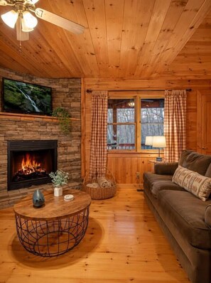 Ein gemütliches Blockhaus-Interieur mit Kamin, Holzwänden, einem Fernseher und einer komfortablen Sitzecke.