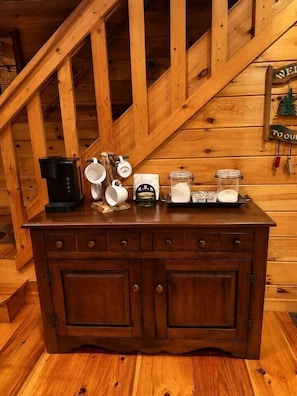 Eine Holztreppe führt in den Innenraum einer Holzhütte, wo ein Küchenschrank mit Küchenutensilien steht.